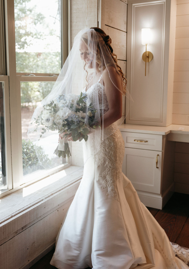 Bride standing by window holding bouquet